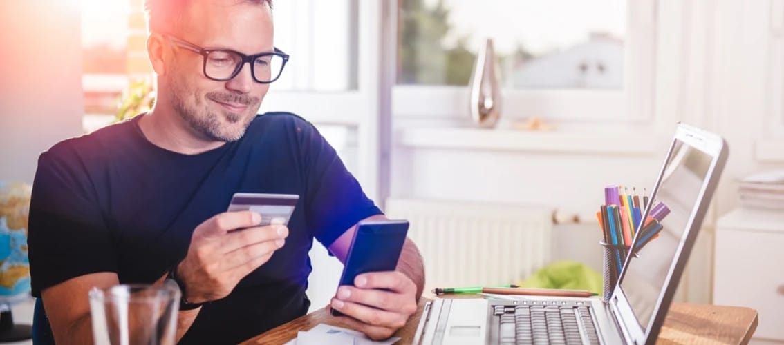 A male physician smiles and looks at his credit card and phone.