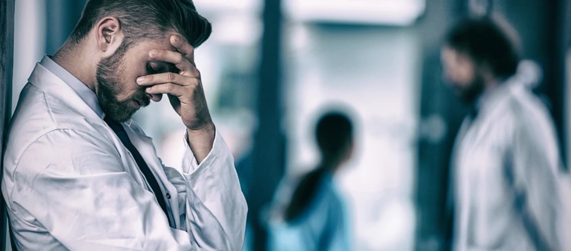 A male physician looks stressed while standing in a hallway