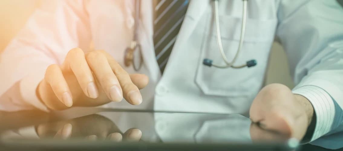 Physician in white coat using tablet.