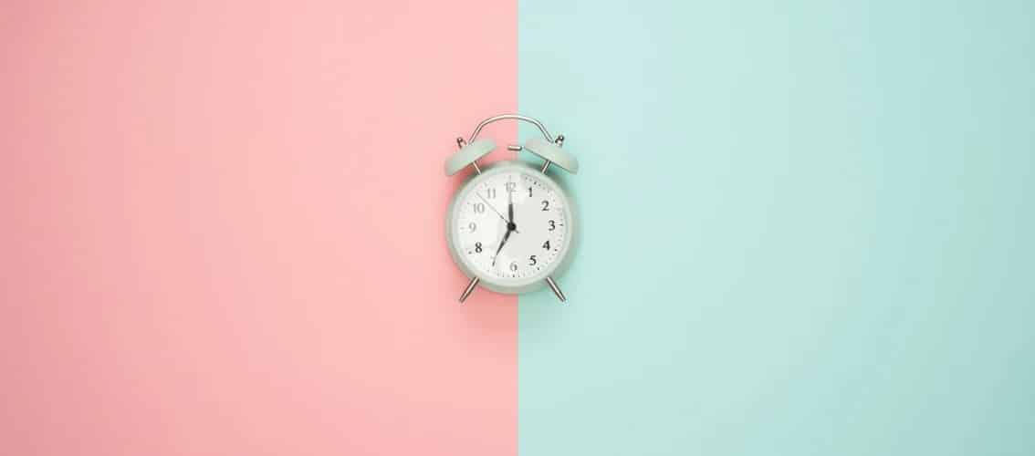 An alarm clock sits on a field of blue and pink.