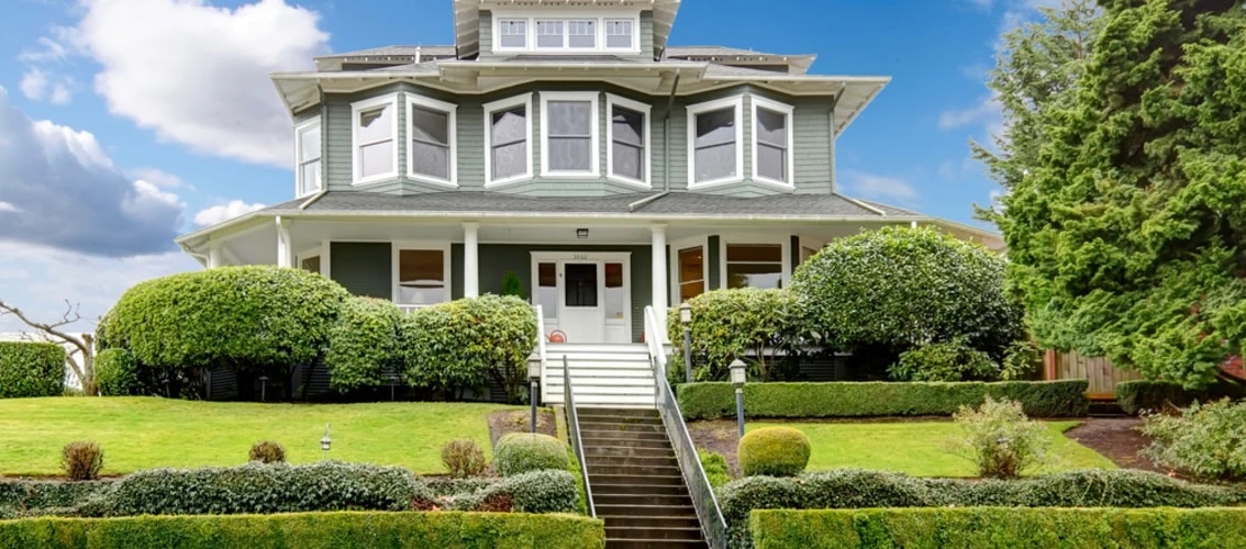 large three story home with wraparound porch and trees