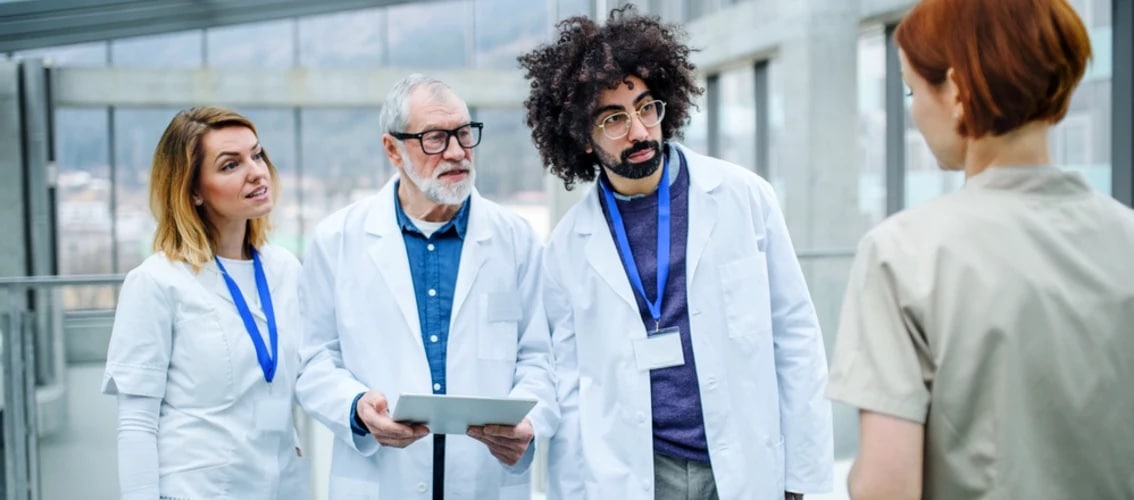Three physicians talk to a nurse in a hospital hallway