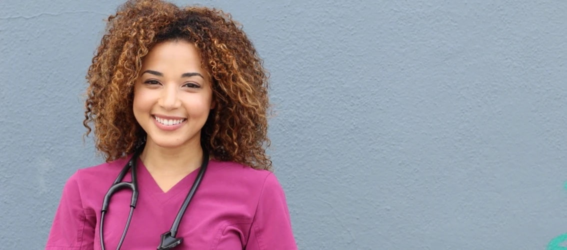 smiling nurse in pink scrubs stands outside