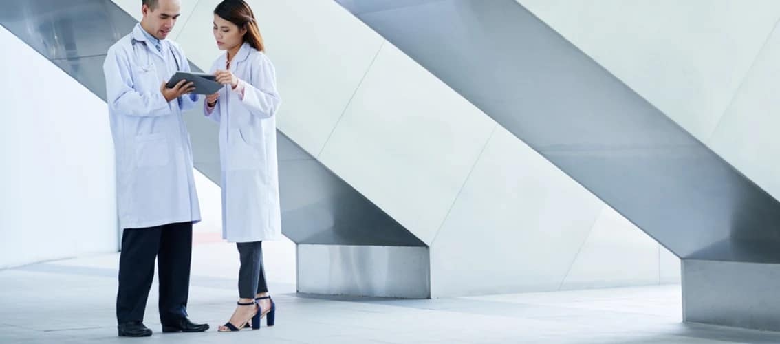 two doctors stand in a hallway and review documents