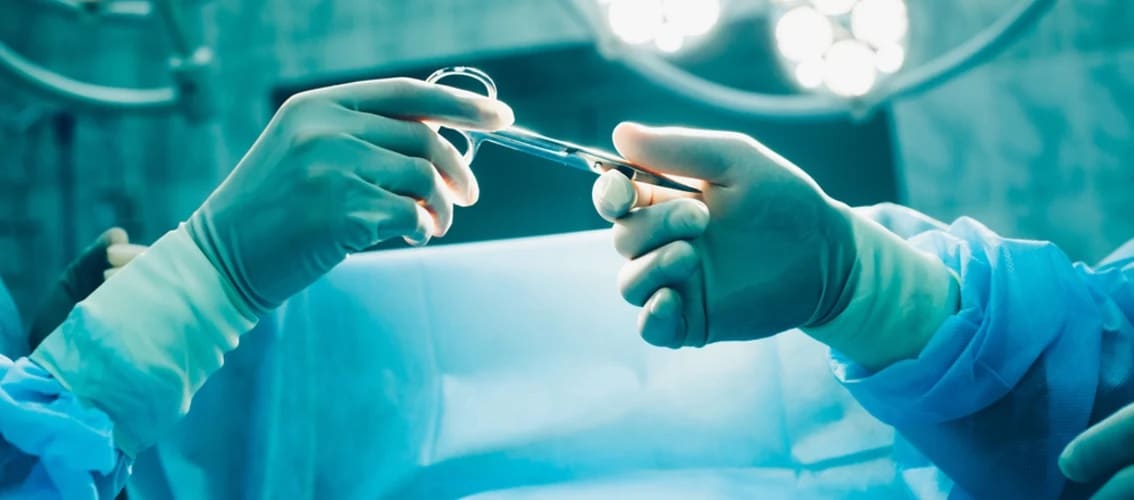 a surgeon hands a pair of forceps to another surgeon