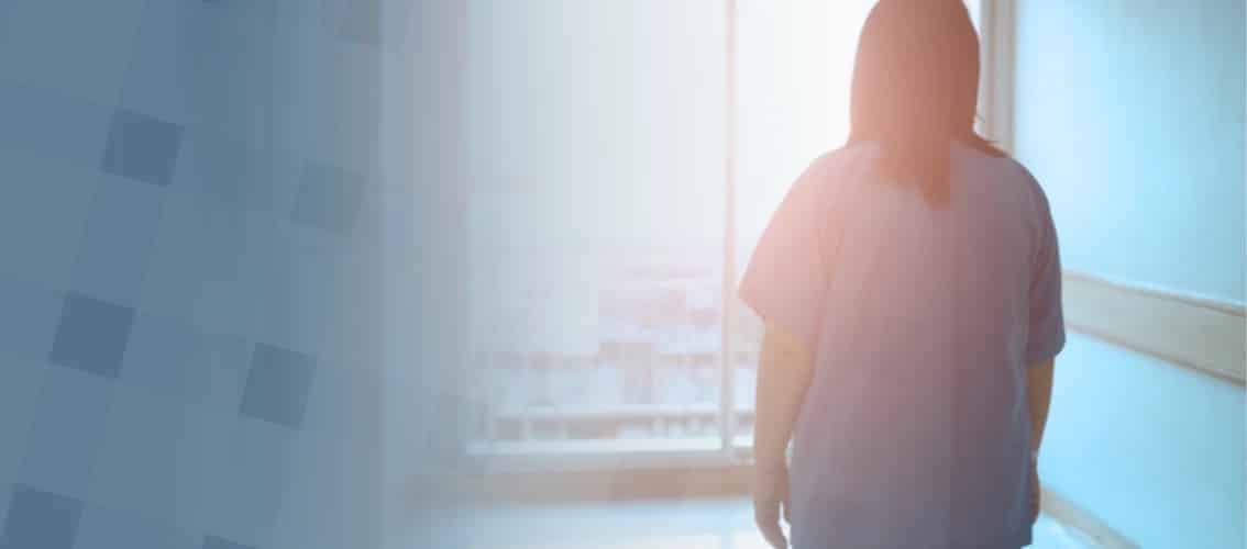 Physician in blue scrubs looks out a hallway window.