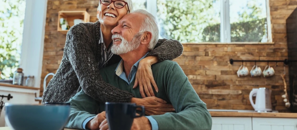 older physician couple looks happy in their kitchen