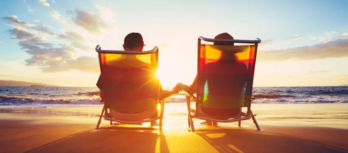 Retired couple sits on beach at sunset