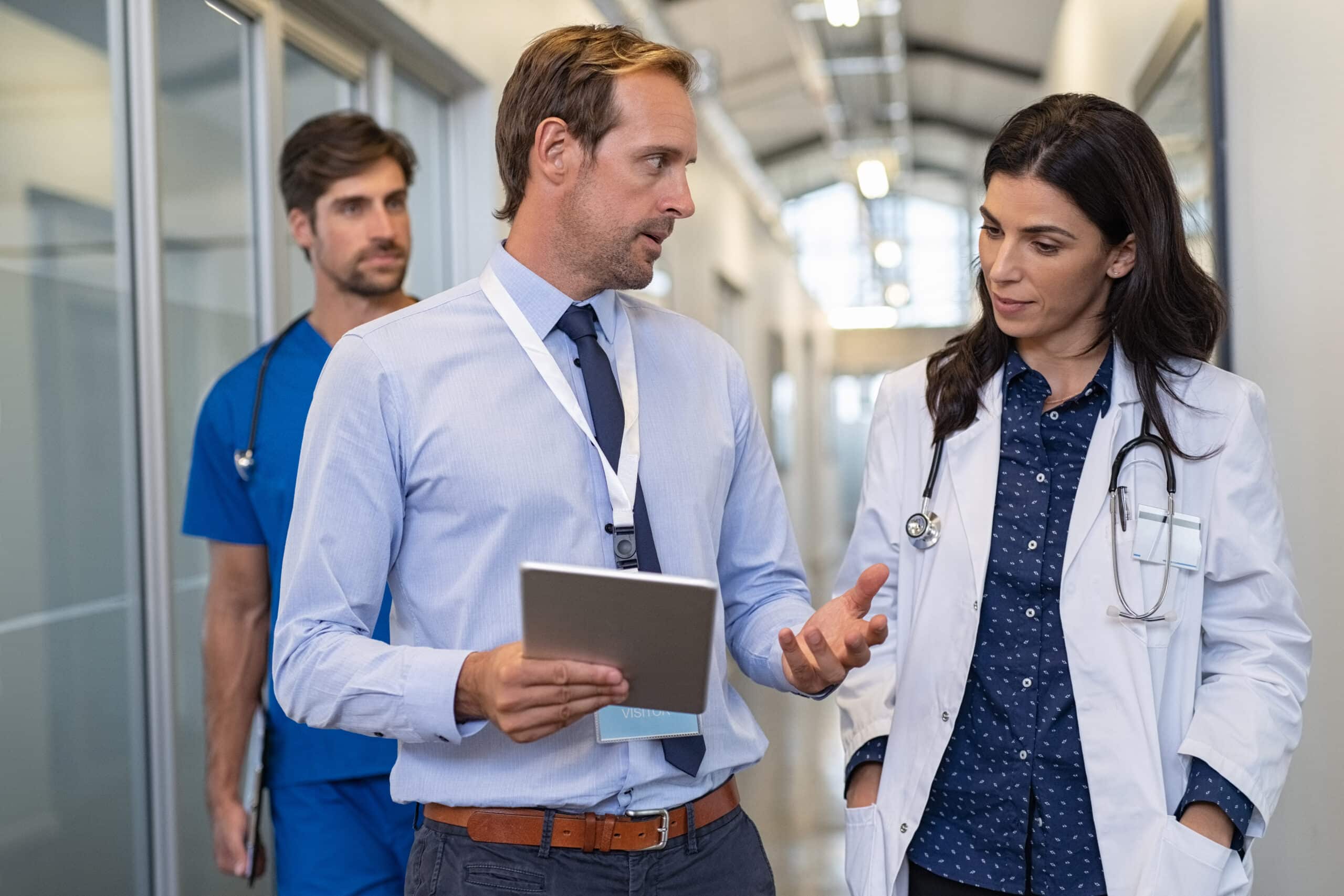 A businessman talks to a physician and a nurse in a hallway.