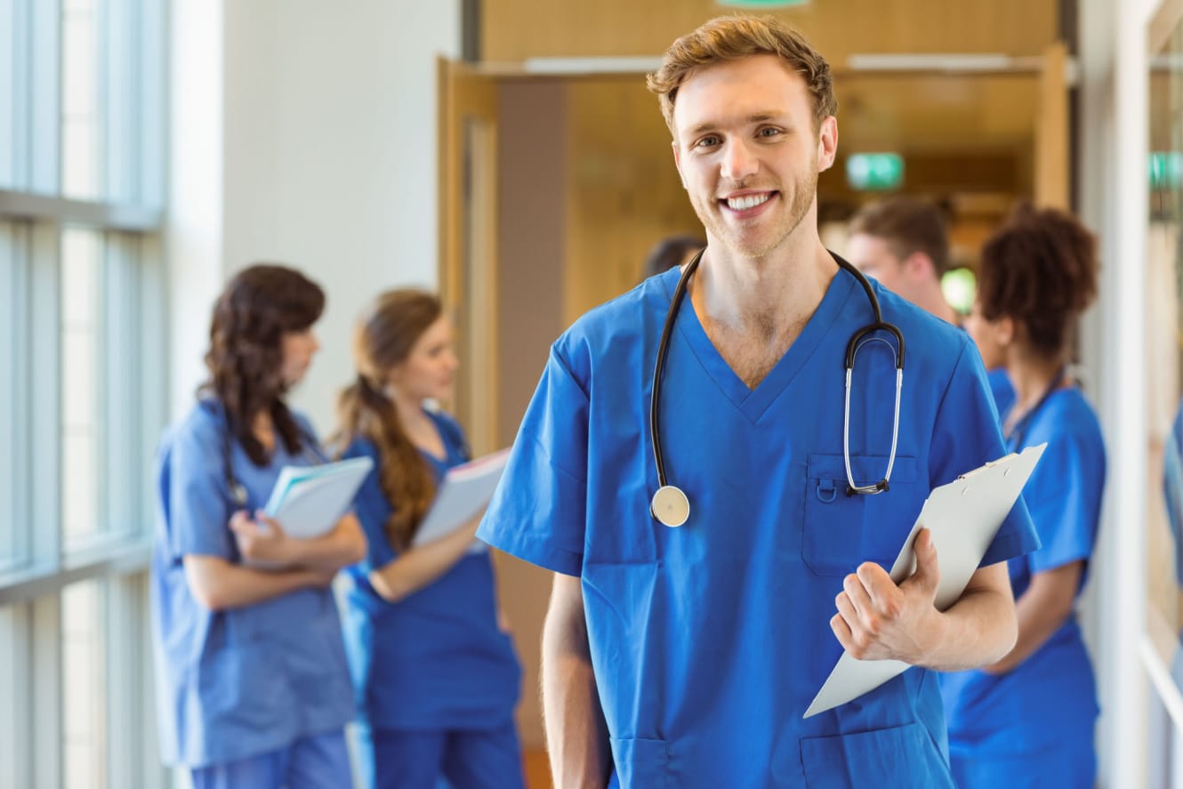 A male resident holds files and smiles in a hallway.