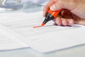 A hand drags an orange highlighter across text on a piece of paper.