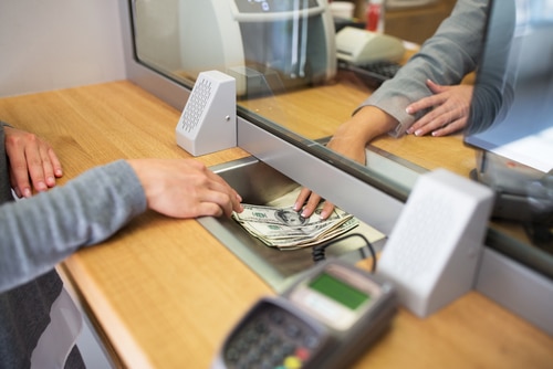 Image shows hands exchanging money at the bank (bank loan)