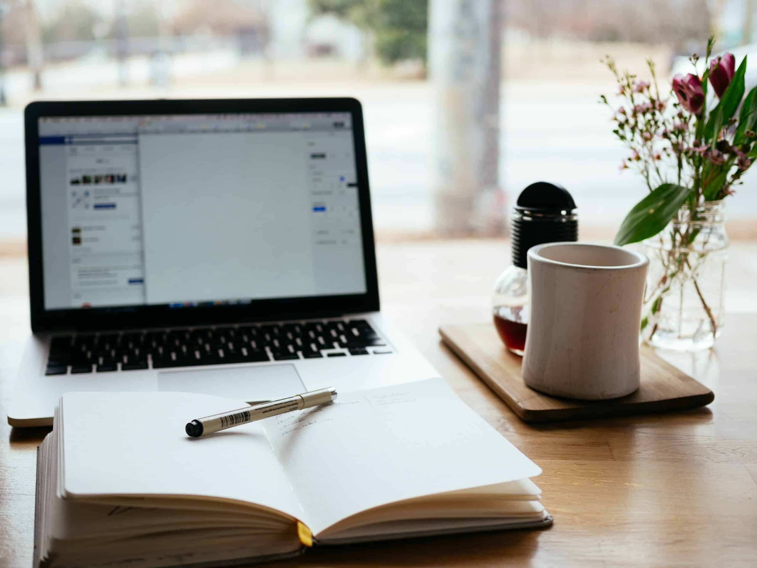 a notebook and laptop sit on a desk near a cup of coffee